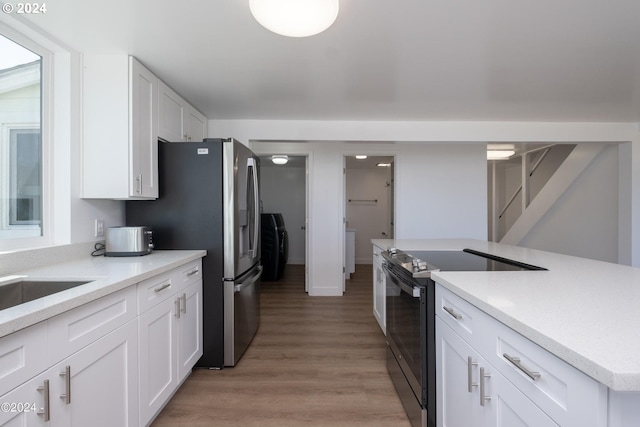 kitchen with light wood-type flooring, sink, washer / dryer, stainless steel appliances, and white cabinetry