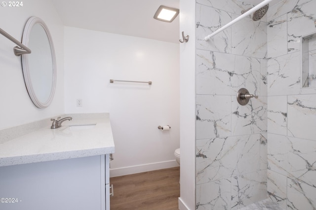 bathroom with hardwood / wood-style flooring, a tile shower, toilet, and vanity