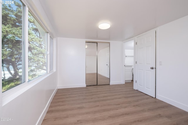 unfurnished bedroom with wood-type flooring, a closet, and multiple windows