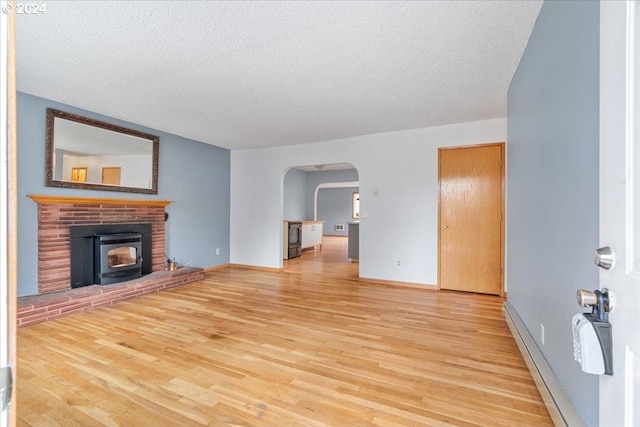 unfurnished living room with light wood-type flooring, a baseboard heating unit, a fireplace, and a textured ceiling