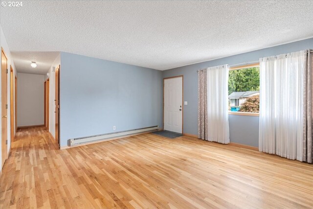 spare room featuring a baseboard radiator, light hardwood / wood-style floors, and a textured ceiling