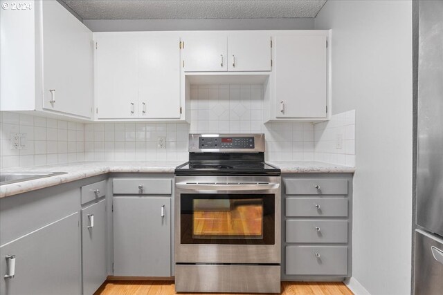 kitchen with light wood-type flooring, white cabinets, backsplash, and stainless steel range with electric cooktop