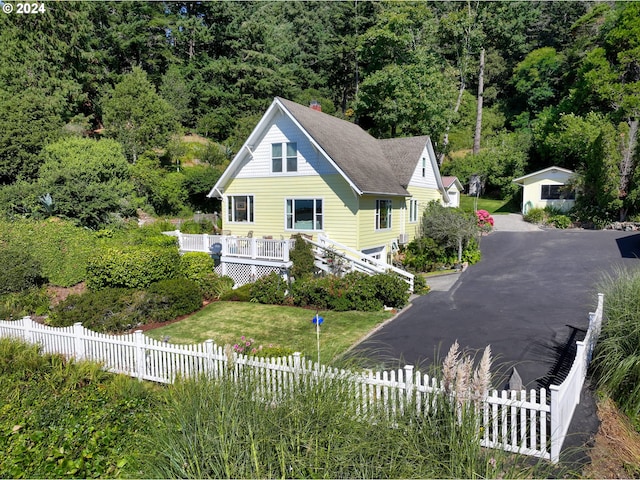 view of side of property featuring driveway, a fenced front yard, a shingled roof, and a yard