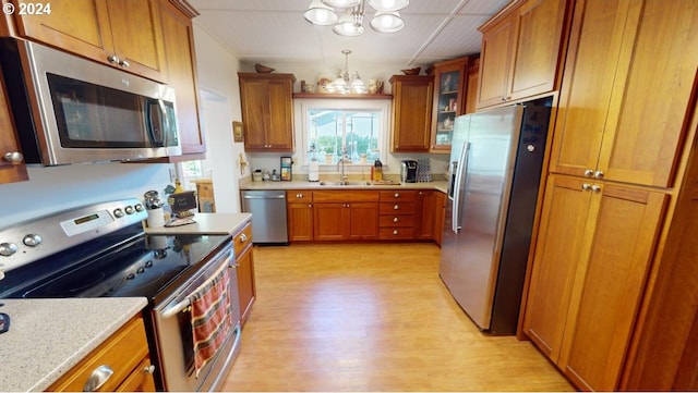 kitchen featuring light stone countertops, stainless steel appliances, light hardwood / wood-style floors, a notable chandelier, and sink