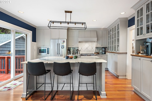 kitchen featuring pendant lighting, appliances with stainless steel finishes, light stone countertops, a center island with sink, and decorative backsplash