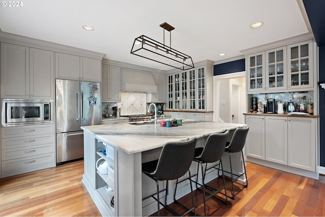 kitchen featuring premium range hood, tasteful backsplash, a center island with sink, appliances with stainless steel finishes, and pendant lighting