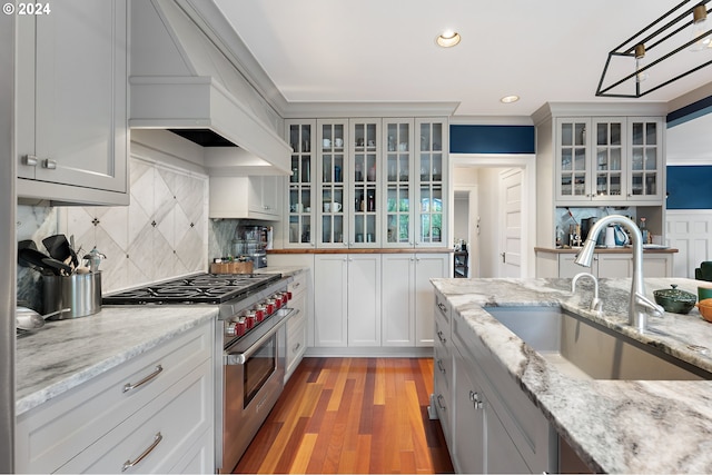 kitchen featuring sink, premium range hood, high end range, tasteful backsplash, and light wood-type flooring