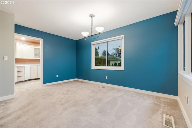 empty room with light carpet and a notable chandelier