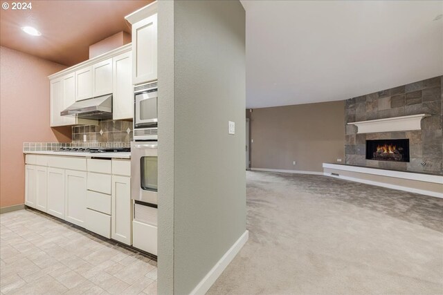 kitchen with appliances with stainless steel finishes, white cabinetry, light carpet, and backsplash