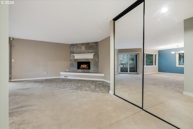 unfurnished living room featuring a large fireplace, a chandelier, and carpet floors