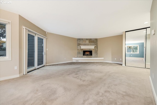 unfurnished living room with a stone fireplace and light colored carpet