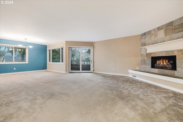 unfurnished living room featuring a notable chandelier, carpet floors, and a tiled fireplace