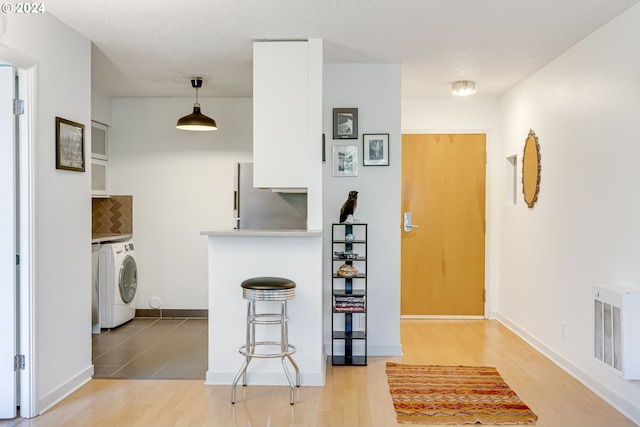 kitchen with white cabinets, pendant lighting, washer / dryer, and light hardwood / wood-style flooring