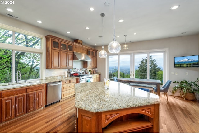 kitchen featuring a center island, wall chimney exhaust hood, pendant lighting, light wood-type flooring, and appliances with stainless steel finishes