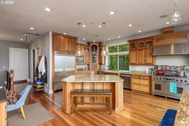 kitchen with a kitchen island, high quality appliances, wall chimney exhaust hood, light stone counters, and light wood-type flooring