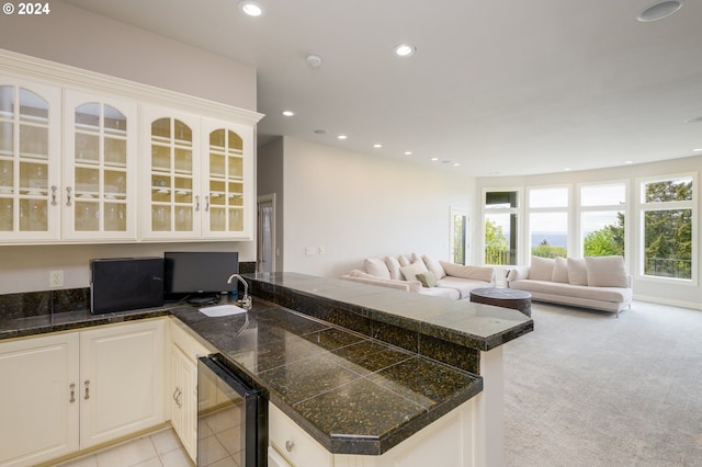 kitchen featuring light colored carpet, sink, kitchen peninsula, and white cabinetry