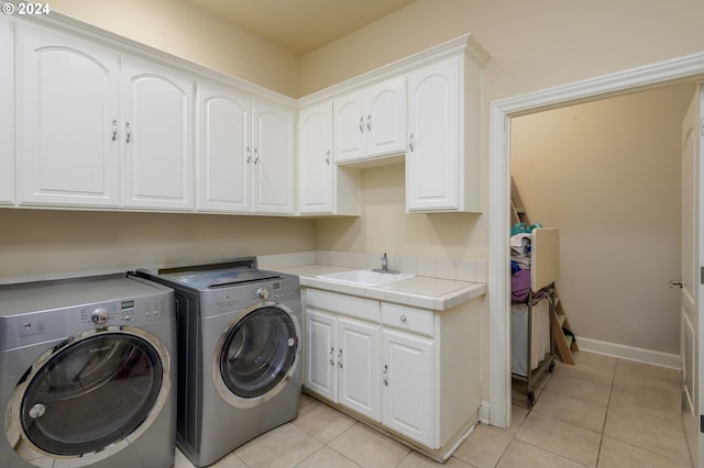 laundry room with washing machine and clothes dryer, cabinets, sink, and light tile flooring