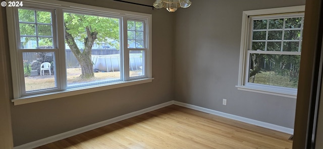 empty room with a notable chandelier, light hardwood / wood-style flooring, and a healthy amount of sunlight