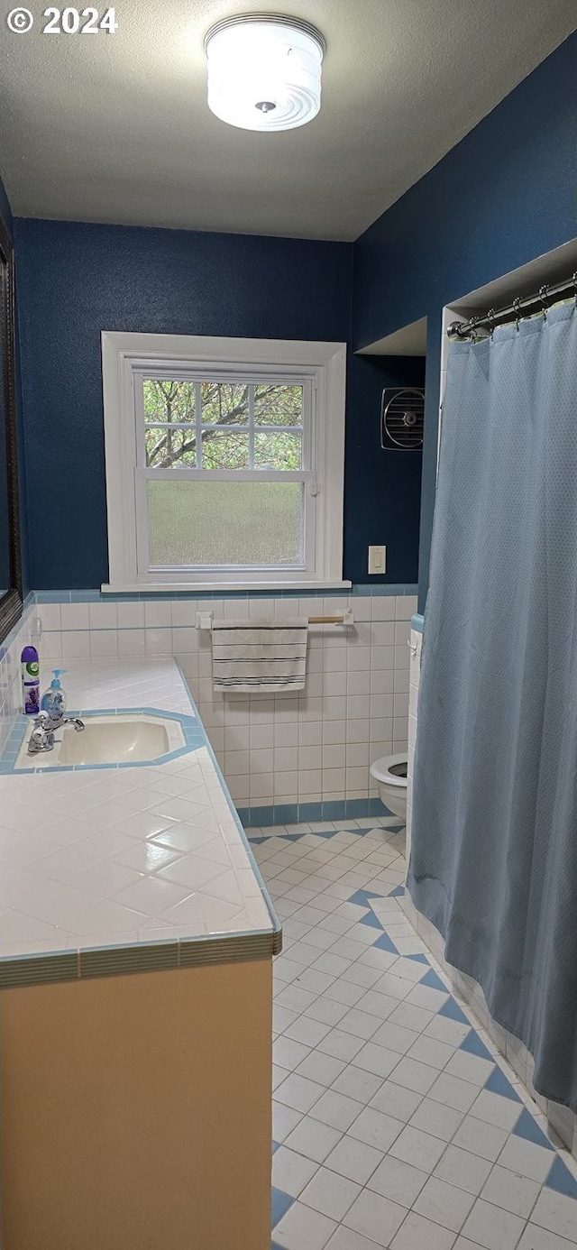 bathroom with tile walls, toilet, vanity, and tile patterned floors