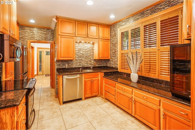 kitchen featuring dark stone counters, light tile patterned flooring, ornamental molding, and stainless steel appliances