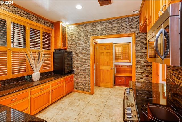 kitchen with dark stone counters, crown molding, stove, and light tile patterned floors