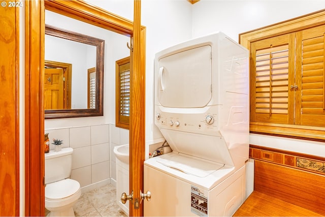 bathroom with tile walls, stacked washer / dryer, toilet, and tile patterned flooring