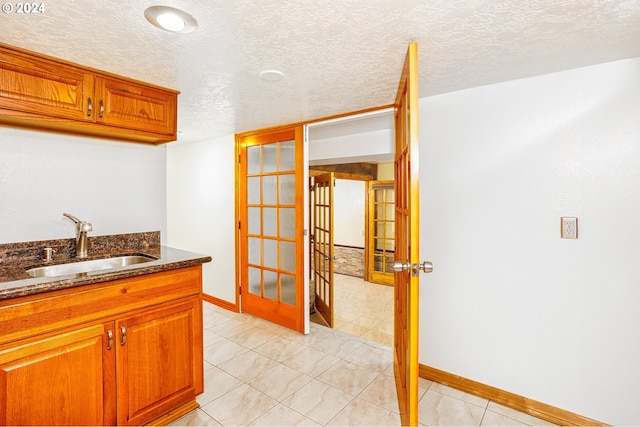 kitchen featuring a textured ceiling, dark stone countertops, sink, and light tile patterned floors