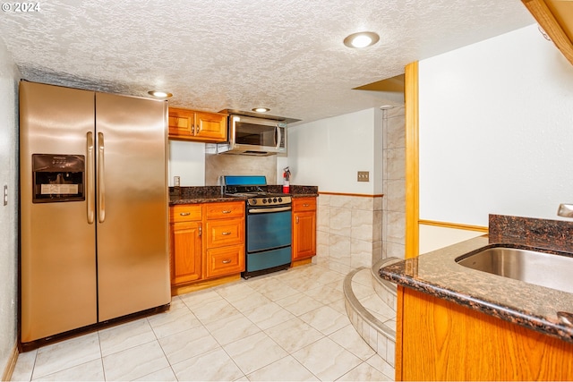 kitchen featuring dark stone countertops, light tile patterned flooring, stainless steel appliances, a textured ceiling, and sink