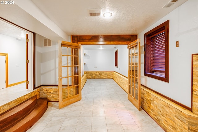 hall with french doors, a textured ceiling, and light tile patterned floors