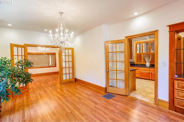 empty room with light wood-type flooring, an inviting chandelier, and french doors