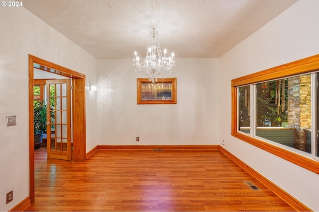 unfurnished room featuring a textured ceiling, light hardwood / wood-style floors, an inviting chandelier, and french doors