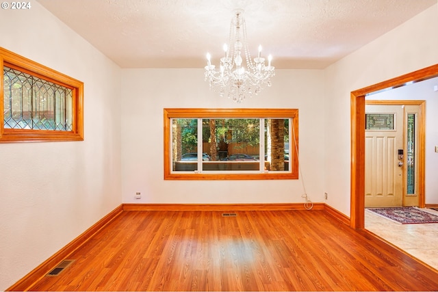 spare room featuring light wood-type flooring, a chandelier, and a textured ceiling