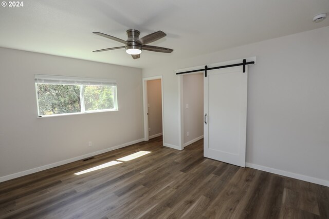 unfurnished bedroom with ceiling fan, hardwood / wood-style flooring, and a barn door