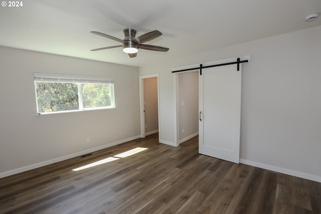 unfurnished bedroom featuring baseboards, a barn door, visible vents, and dark wood-style flooring