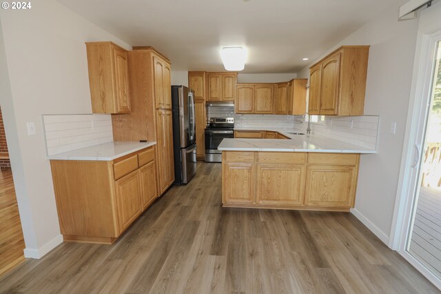 kitchen with light hardwood / wood-style floors, appliances with stainless steel finishes, kitchen peninsula, and decorative backsplash