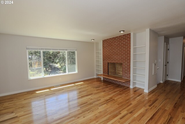 unfurnished living room featuring a fireplace, brick wall, and light hardwood / wood-style floors