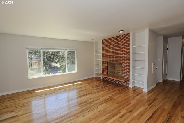 unfurnished living room with built in features, a brick fireplace, baseboards, and wood finished floors