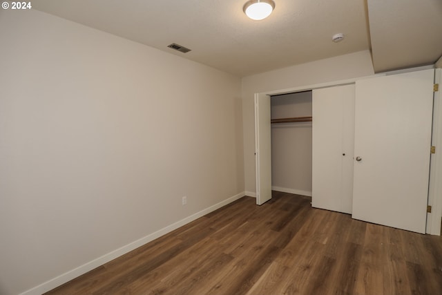 unfurnished bedroom featuring dark wood-style floors, baseboards, visible vents, and a closet