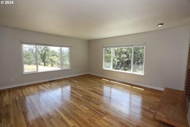 empty room featuring visible vents, a healthy amount of sunlight, light wood-style flooring, and baseboards