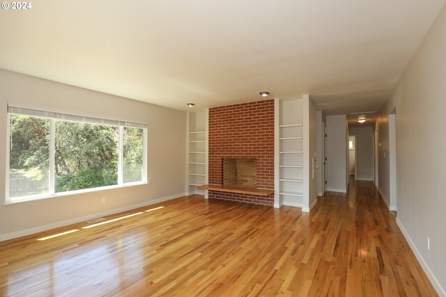 unfurnished living room with brick wall, light hardwood / wood-style floors, and a brick fireplace