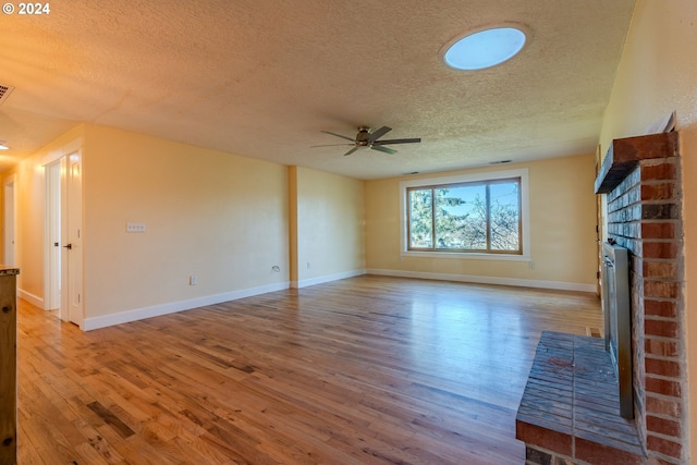 unfurnished living room featuring ceiling fan, wood-type flooring, a textured ceiling, and a brick fireplace