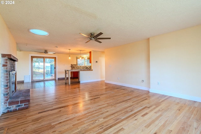 unfurnished living room with ceiling fan, a fireplace, a textured ceiling, and light hardwood / wood-style flooring