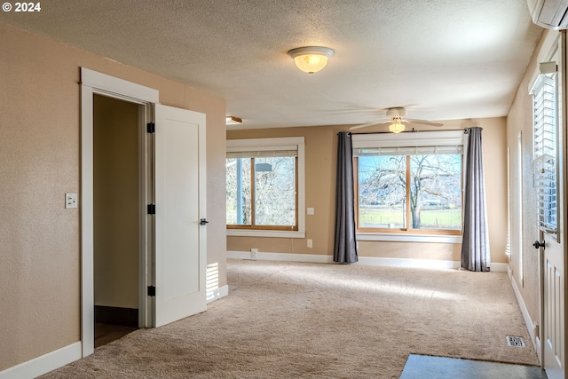 carpeted spare room with a textured ceiling, an AC wall unit, ceiling fan, and a healthy amount of sunlight