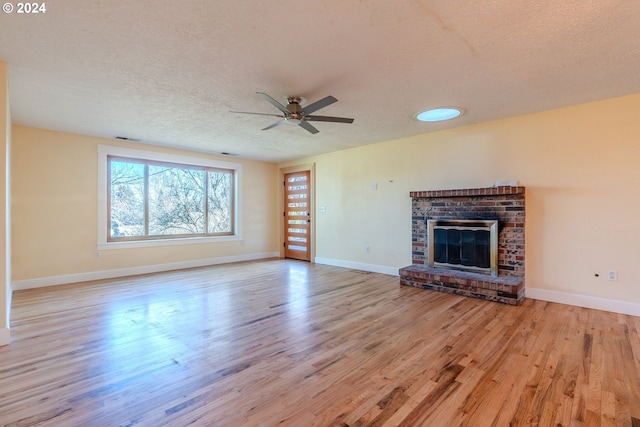 unfurnished living room featuring ceiling fan, a fireplace, a textured ceiling, and light wood-type flooring