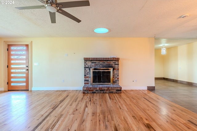 unfurnished living room featuring hardwood / wood-style flooring, ceiling fan, a textured ceiling, and a brick fireplace