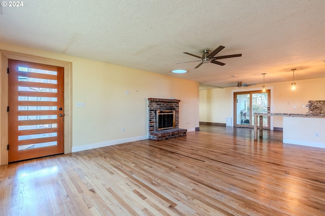 unfurnished living room featuring a fireplace, a textured ceiling, light hardwood / wood-style floors, and ceiling fan