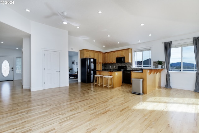 kitchen featuring light hardwood / wood-style floors, lofted ceiling, a breakfast bar area, a kitchen island, and black appliances