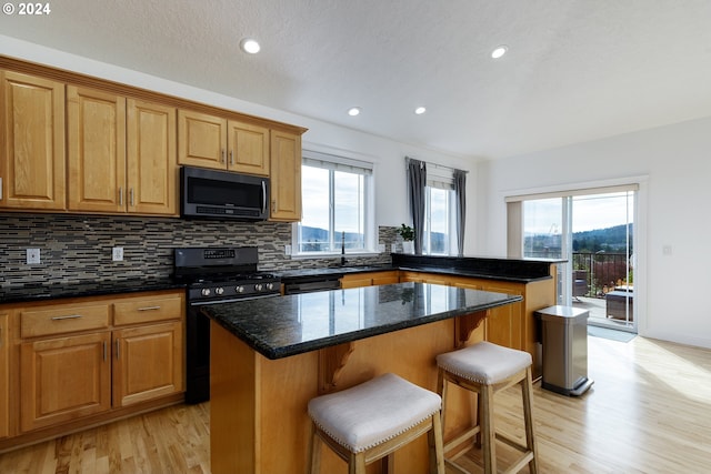 kitchen with black stove, light wood-type flooring, a kitchen breakfast bar, dark stone countertops, and a kitchen island