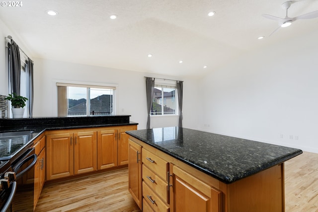 kitchen with ceiling fan, dark stone counters, light hardwood / wood-style floors, lofted ceiling, and a kitchen island