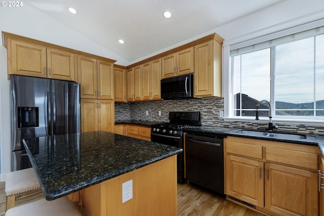 kitchen with a center island, sink, dark stone countertops, vaulted ceiling, and black appliances